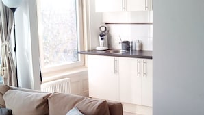 A modern living room with a beige sofa and a dining area with white cabinets and a black countertop. - Apartment in Rotterdam (Rotterdam)
