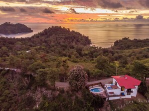 Ein Haus mit rotem Dach, einem Swimmingpool und Blick auf den Ozean im Sonnenuntergang.
