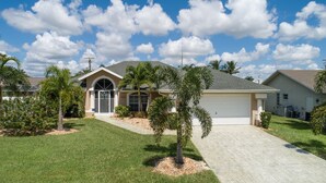 A residential house with a garage, a well-maintained lawn, and a clear sky. - Villa Spain - Family Oasis in the Most Sought Area of Cape Coral (Cape Coral)
