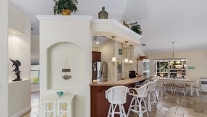 A spacious kitchen with a central island, white bar stools, and a dining area with a table and chairs. - Villa Spain - Family Oasis in the Most Sought Area of Cape Coral (Cape Coral)