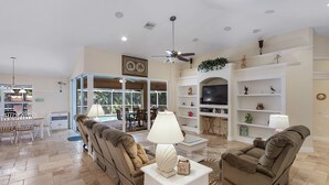 A spacious living room with a sofa, a recliner, a coffee table, and a TV. There is a dining area with chairs and a table, and a kitchen area with a refrigerator and shelves. - Villa Spain - Family Oasis in the Most Sought Area of Cape Coral (Cape Coral)