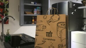 A kitchen with a stainless steel refrigerator, a sink with a faucet, and a shelf with various items including a box of snacks. A brown paper bag with the word "Cornershop" is placed on the counter. - Mexican Bohemian Loft (Queretaro)
