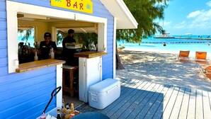 A beachside bar with a sign reading "AB'S BAR" and a view of the beach and ocean in the background.