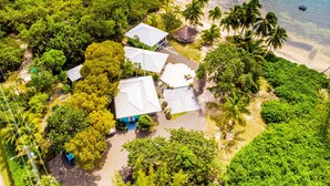 Vue aérienne d’un complexe hôtelier tropical comprenant plusieurs bâtiments, une plage et des palmiers.