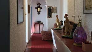Un couloir avec un tapis rouge, un plafond en bois et un mur blanc. On y voit des tableaux encadrés et une lampe décorative accrochée au mur.