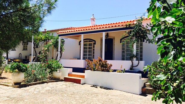 Une maison à deux étages, avec un toit recouvert de tuiles rouges, des murs blancs et une véranda.