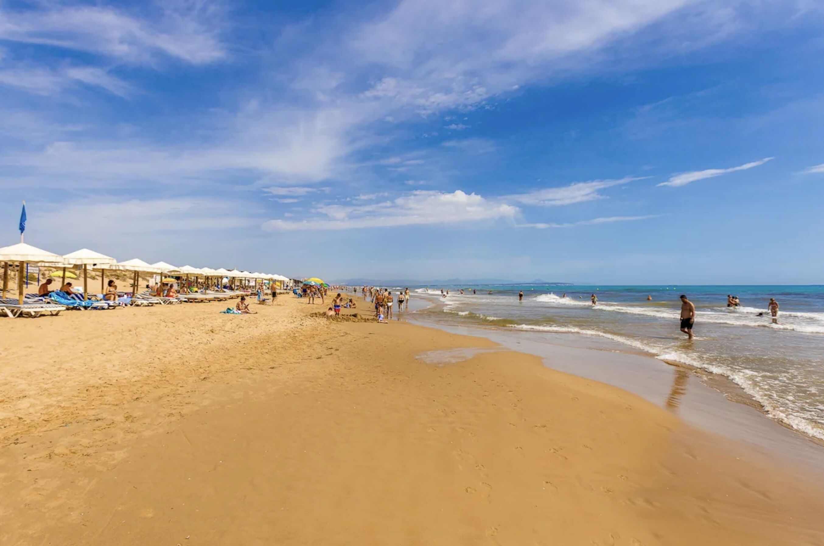 Een strand met ligbedden en parasols, een zandstrand en de oceaan.