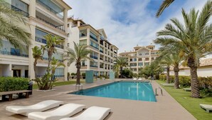 Ein Hotelpoolbereich mit Liegestühlen, Palmen und blauem Himmel.