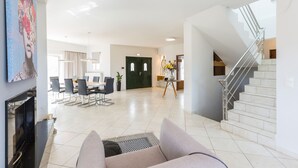A spacious living area with a dining table, chairs, a sofa, a staircase, and a fireplace.