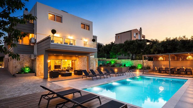 A modern poolside area with lounge chairs, a pool, and a well-lit outdoor seating area.