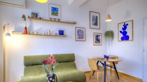 Ein modernes Wohnzimmer mit einem grünen Sofa, einem Couchtisch mit einem Buch, einem kleinen runden Tisch mit einer Vase und verschiedenen gerahmten Kunstwerken an den Wänden.