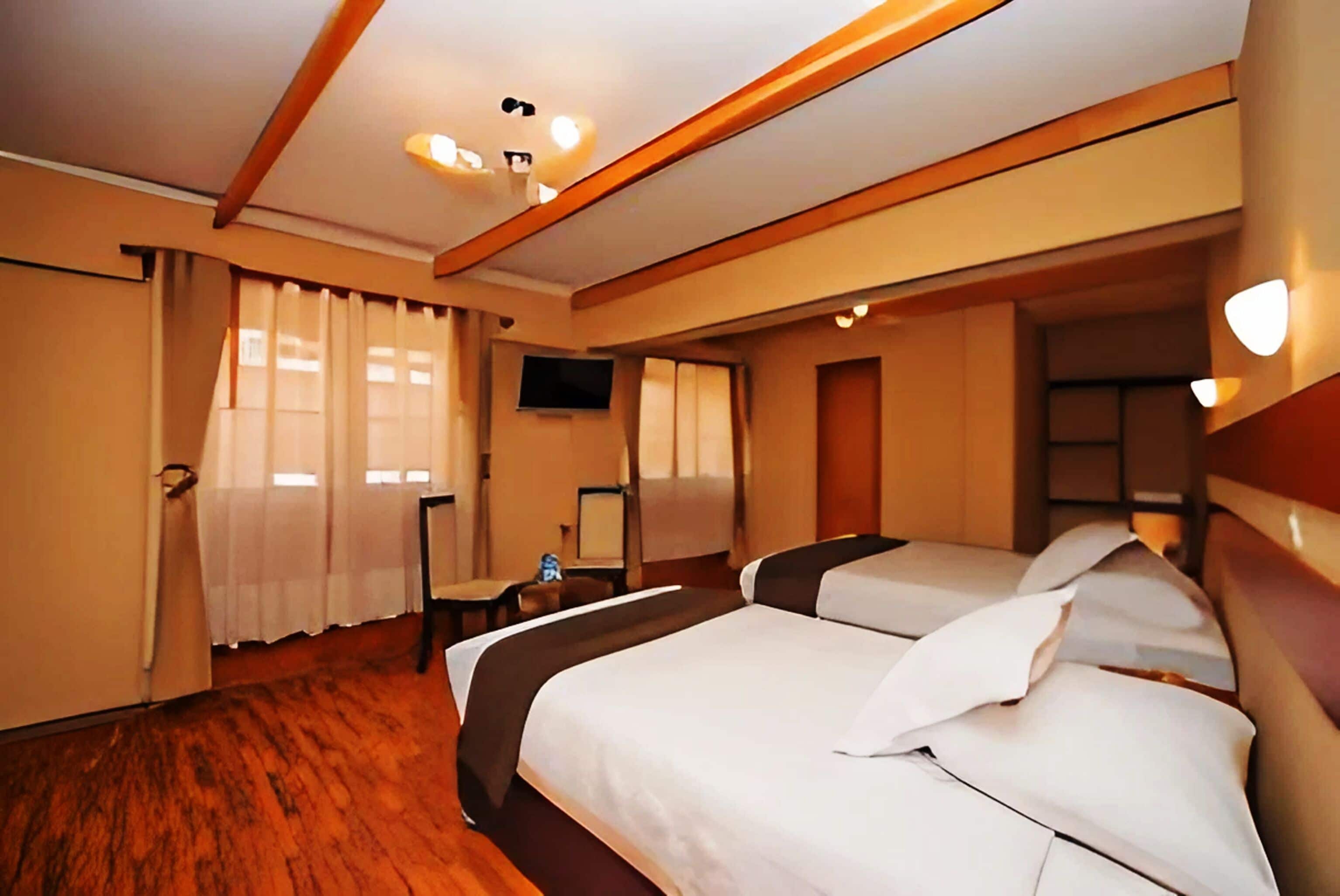 A hotel room with two beds, a television, and a wooden floor.