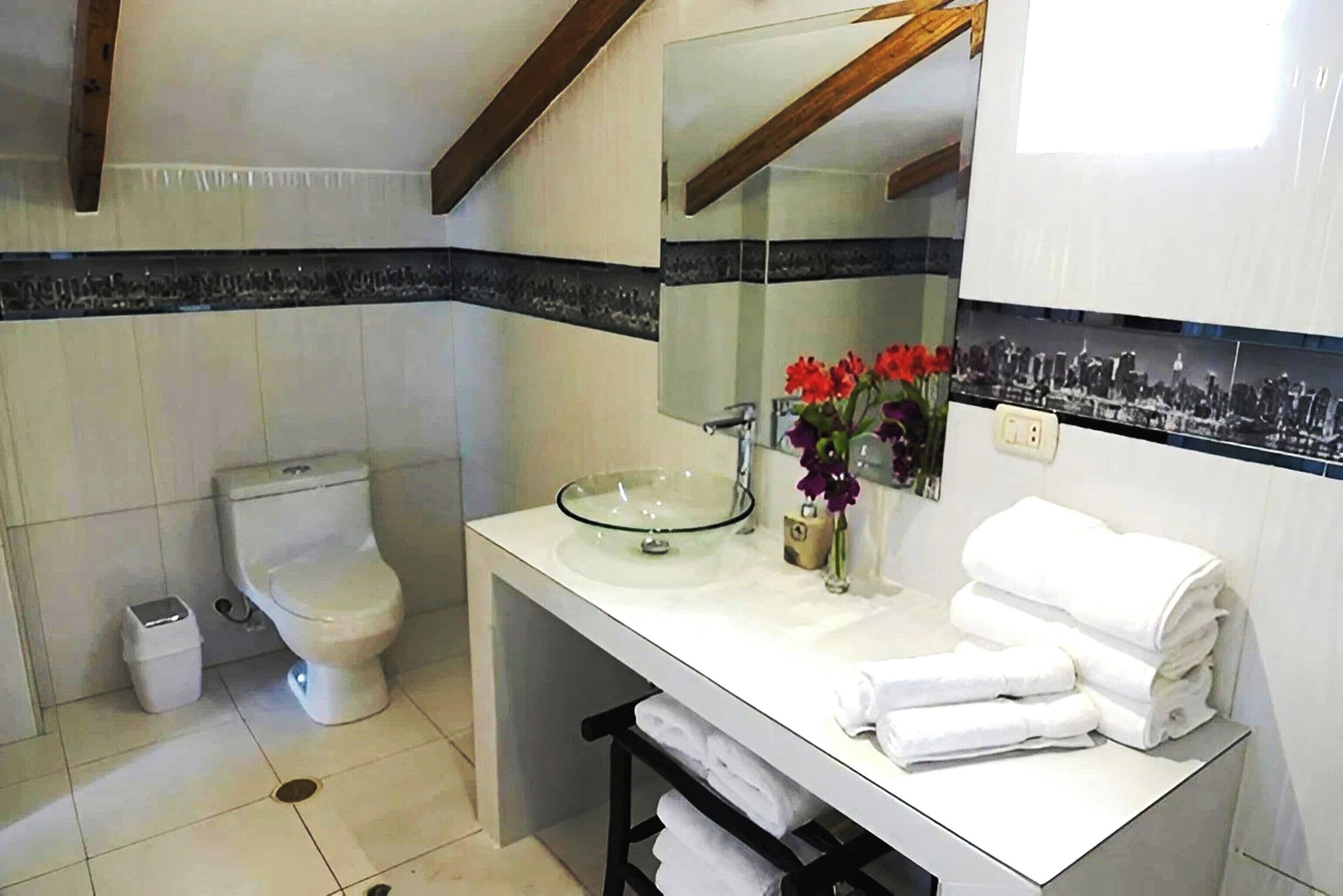 Un baño moderno con lavamanos de vidrio, azulejos blancos, un inodoro y un espejo con marco negro.