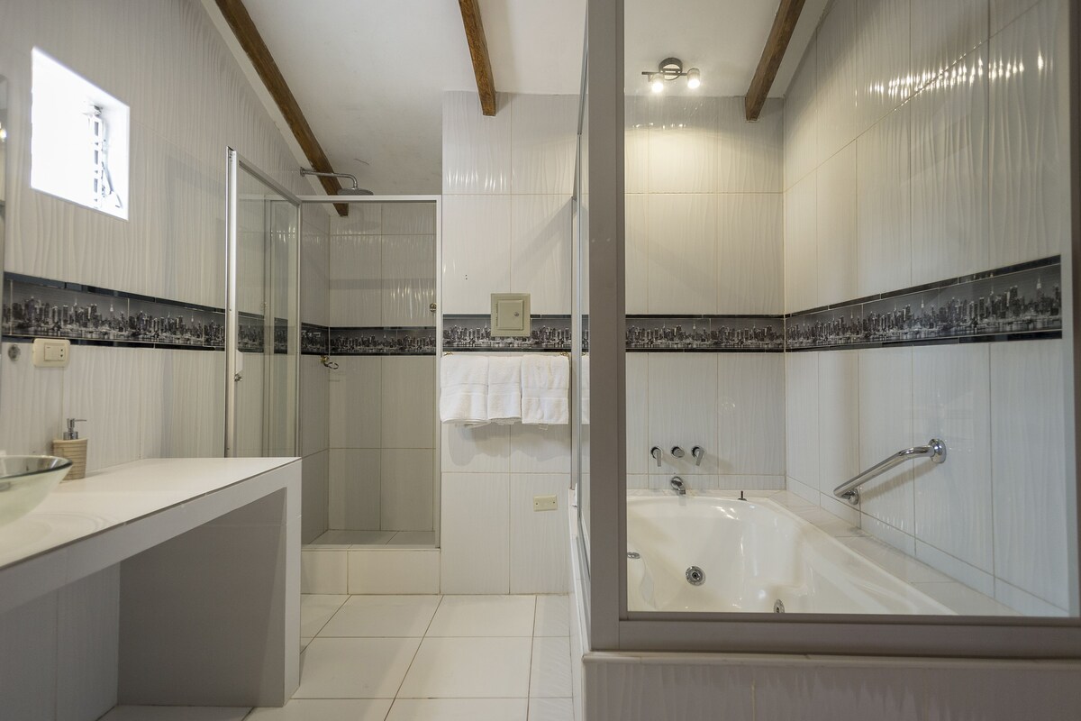 A modern bathroom with a glass shower enclosure, a large bathtub, and a cityscape tile backsplash.