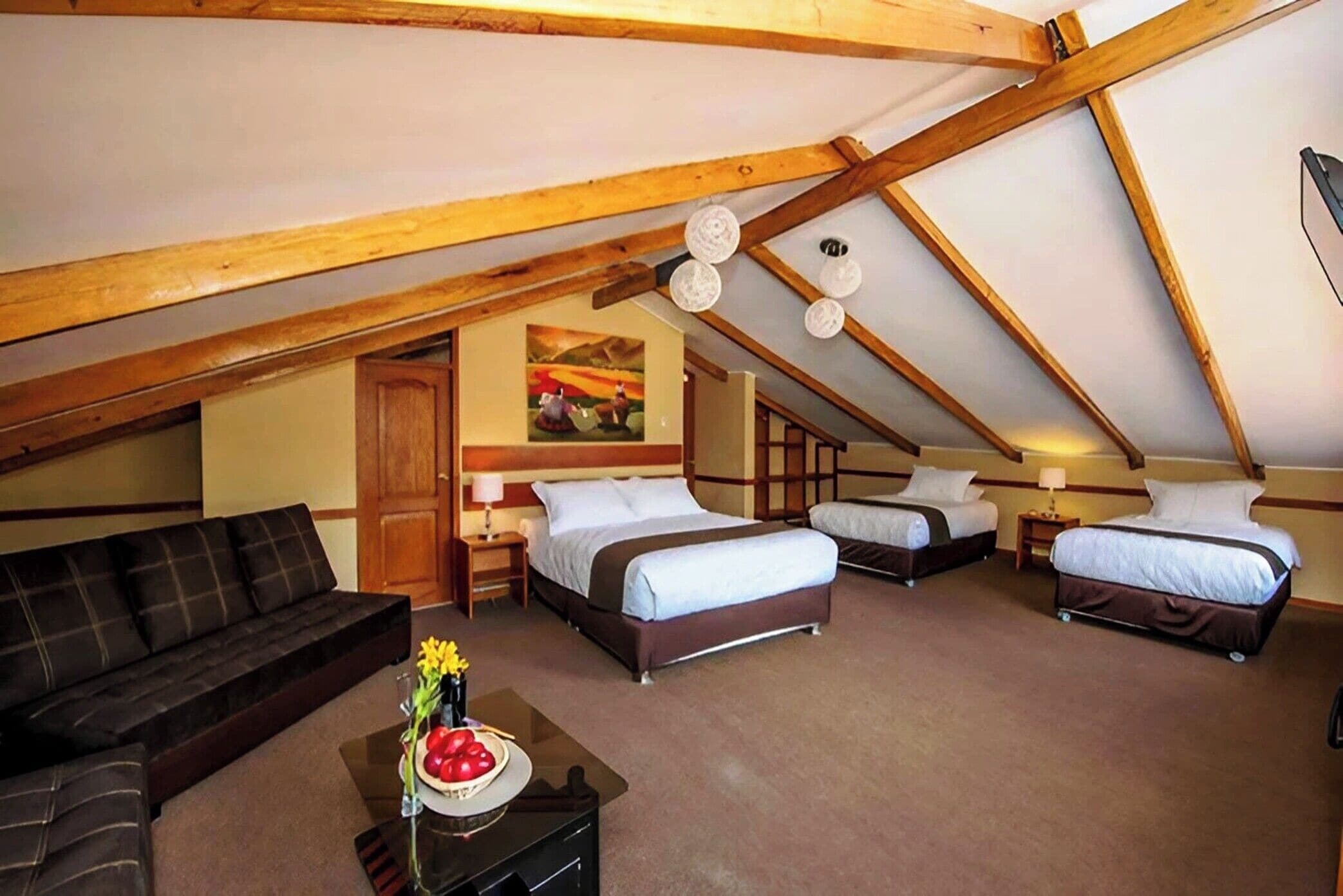 A cozy attic bedroom with a loft-style ceiling, a sofa, two single beds, and a dining table with fruit.