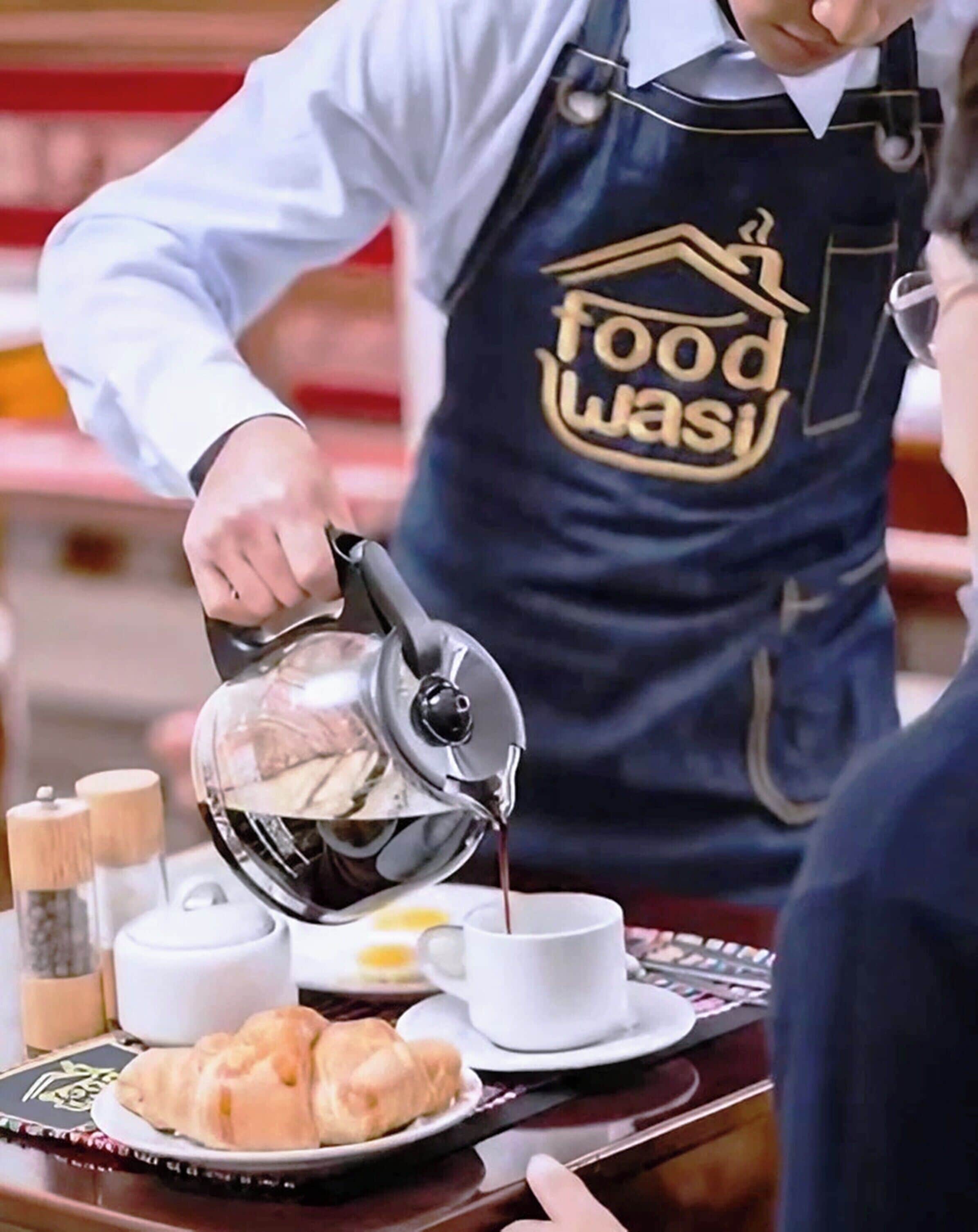 A person pouring coffee into a cup, with a tray containing croissants and condiments.