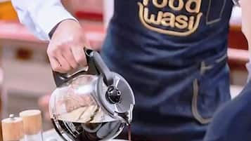 A person pouring coffee into a cup, with a tray containing croissants and condiments.