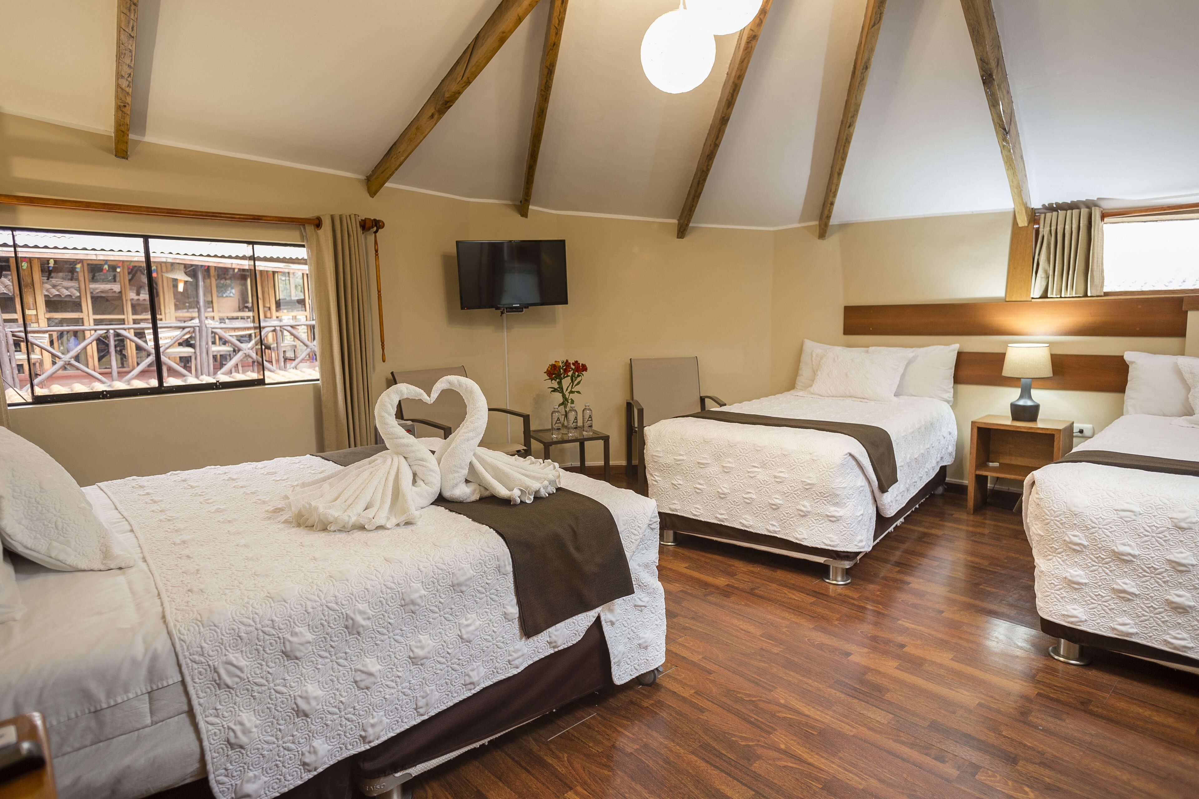 A hotel room with two beds, a TV, and a window with a view of a balcony.
