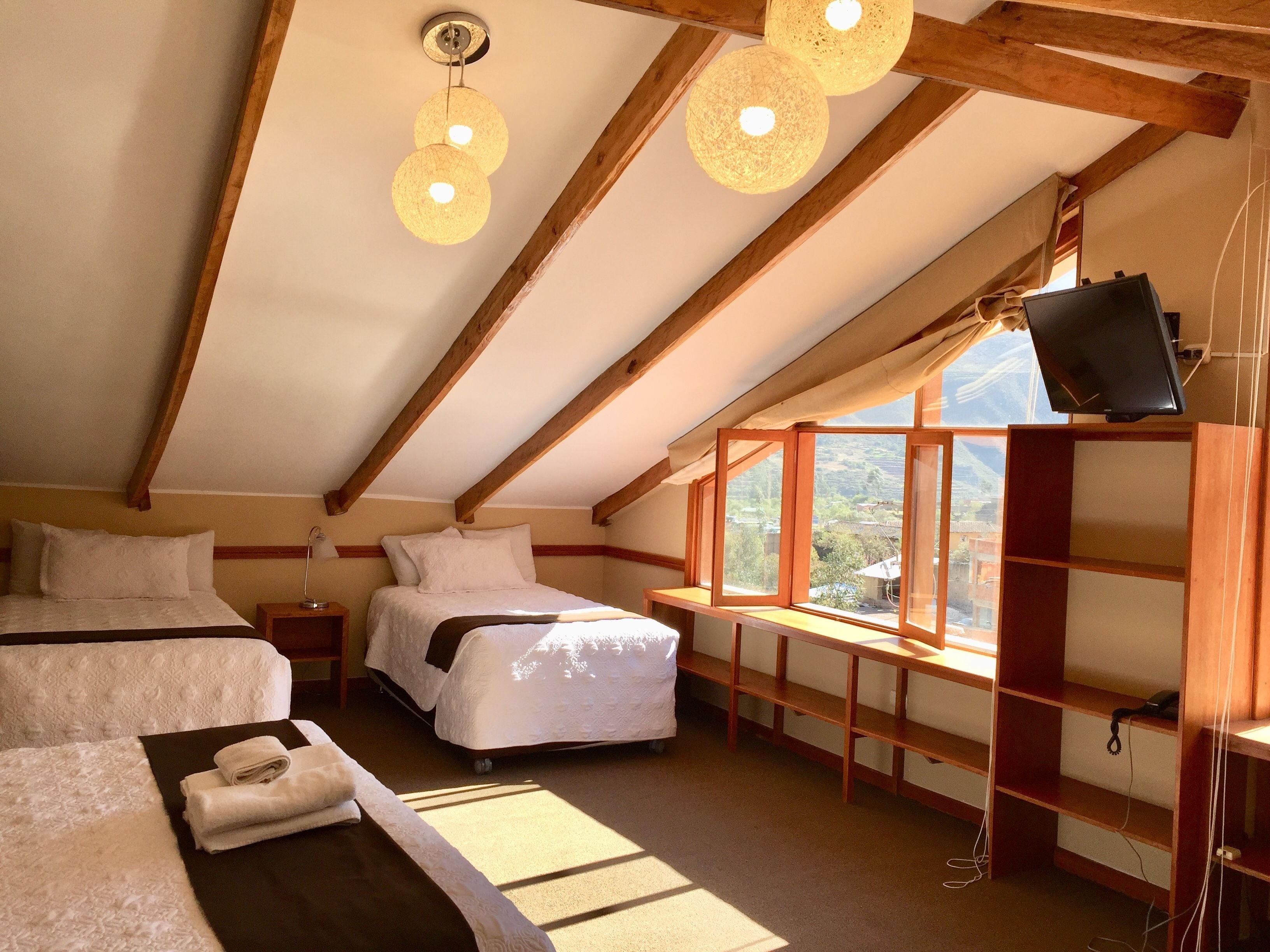Une chambre avec deux lits, un téléviseur fixé au mur et une fenêtre donnant sur l’extérieur.