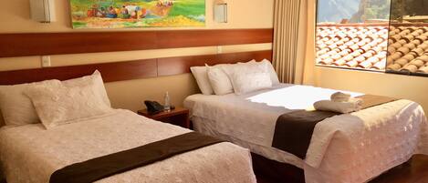 Quarto de hotel com duas camas, um quadro na parede, uma janela com vista para um telhado de azulejos e uma cabeceira de madeira.