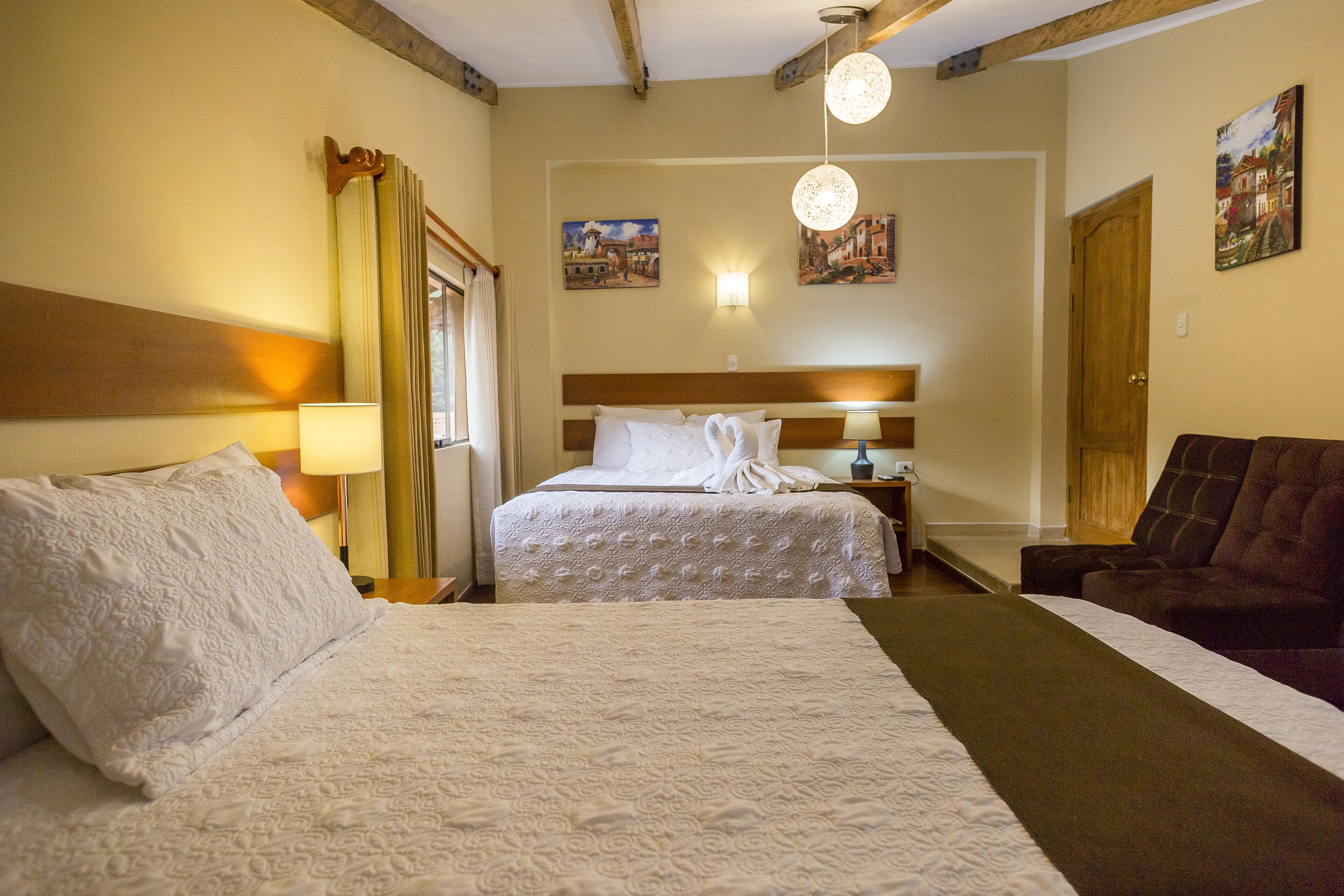 Ein Hotelzimmer mit einem großen Bett, einem kleineren Bett, einer Schlafcouch, einer Lampe, einem Gemälde und einer Tür.