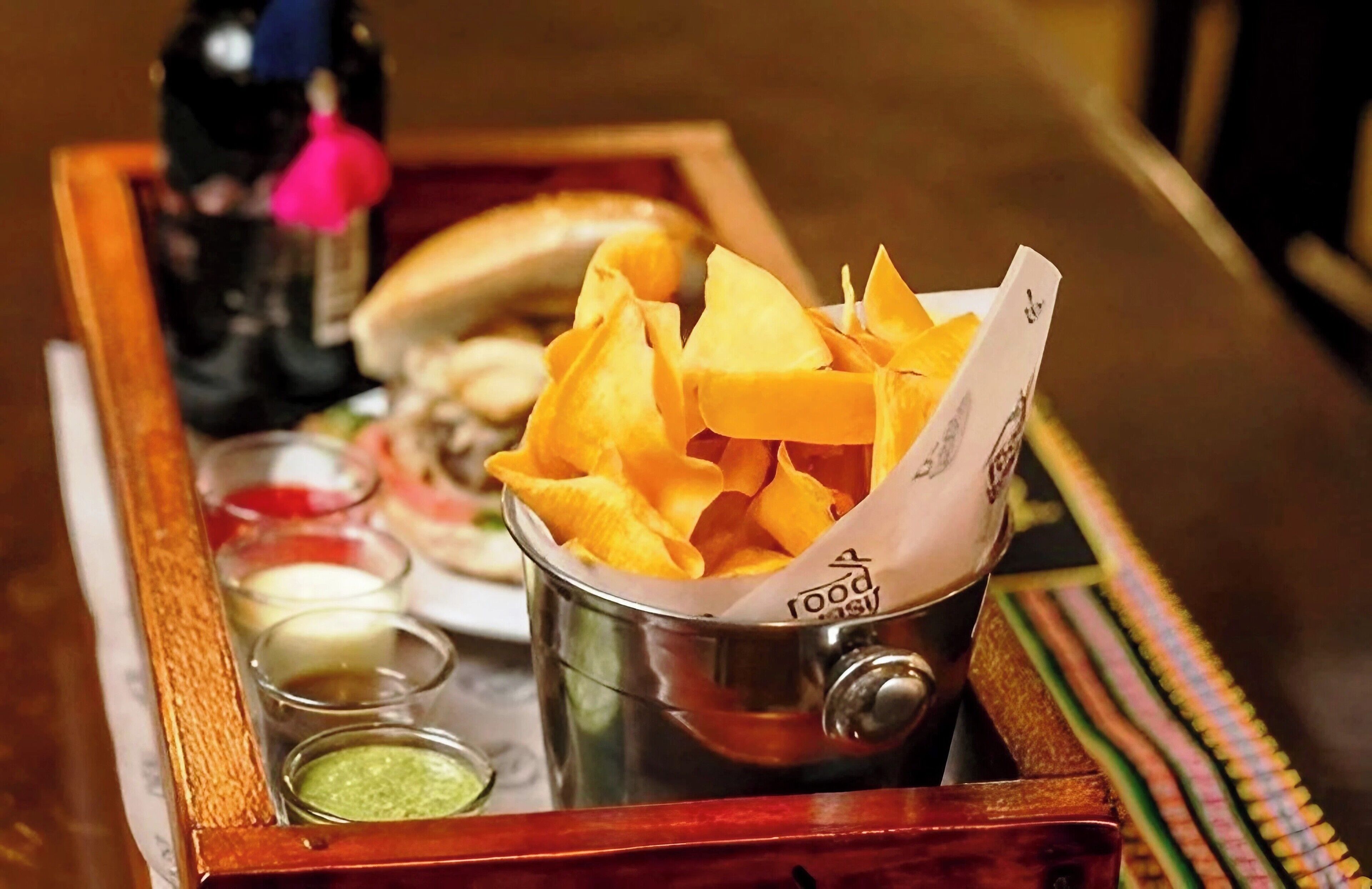En bakke med chips, en sandwich og små beholdere med saucer.