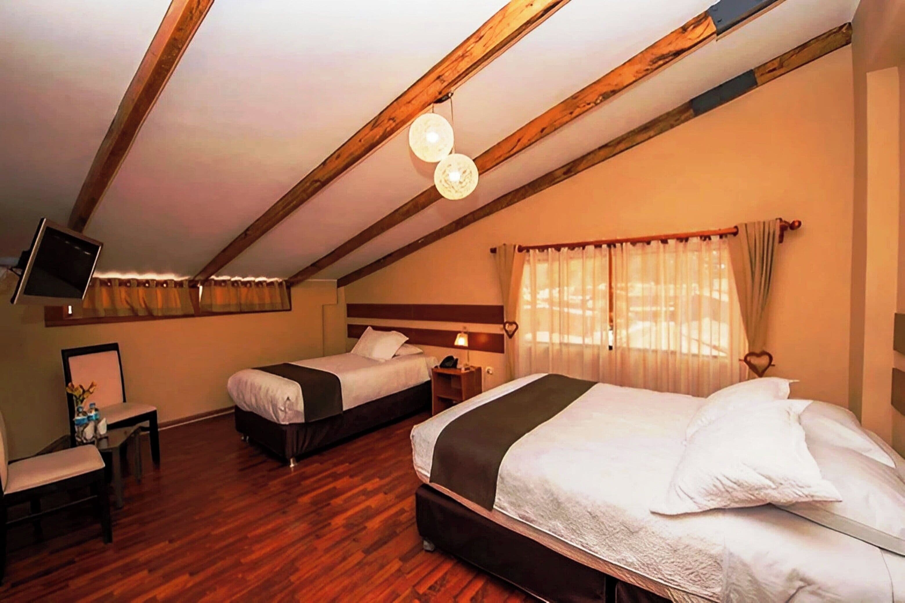 Habitación de hotel con dos camas, vigas de madera en el techo, un televisor de pantalla plana, un escritorio y una ventana con cortinas.