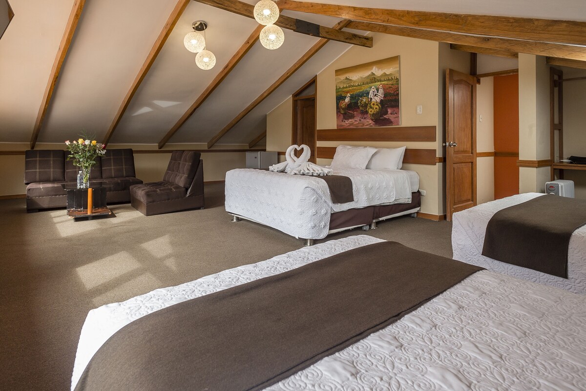 A hotel room with a lofted ceiling, a bed with a heart-shaped decoration, a sofa, and a painting on the wall.