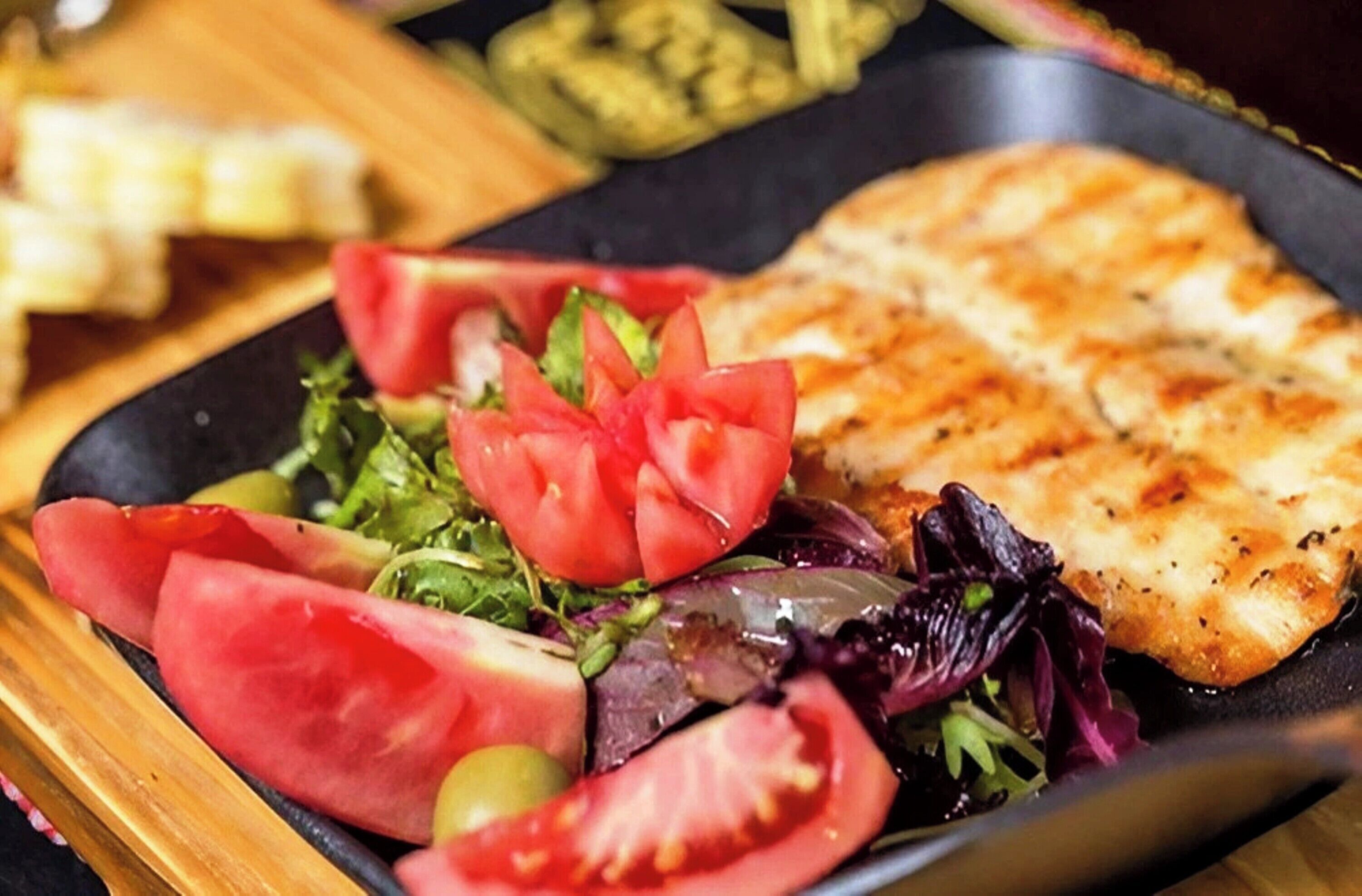 A plate with grilled fish, a salad with tomatoes and greens, and a side of pickles.