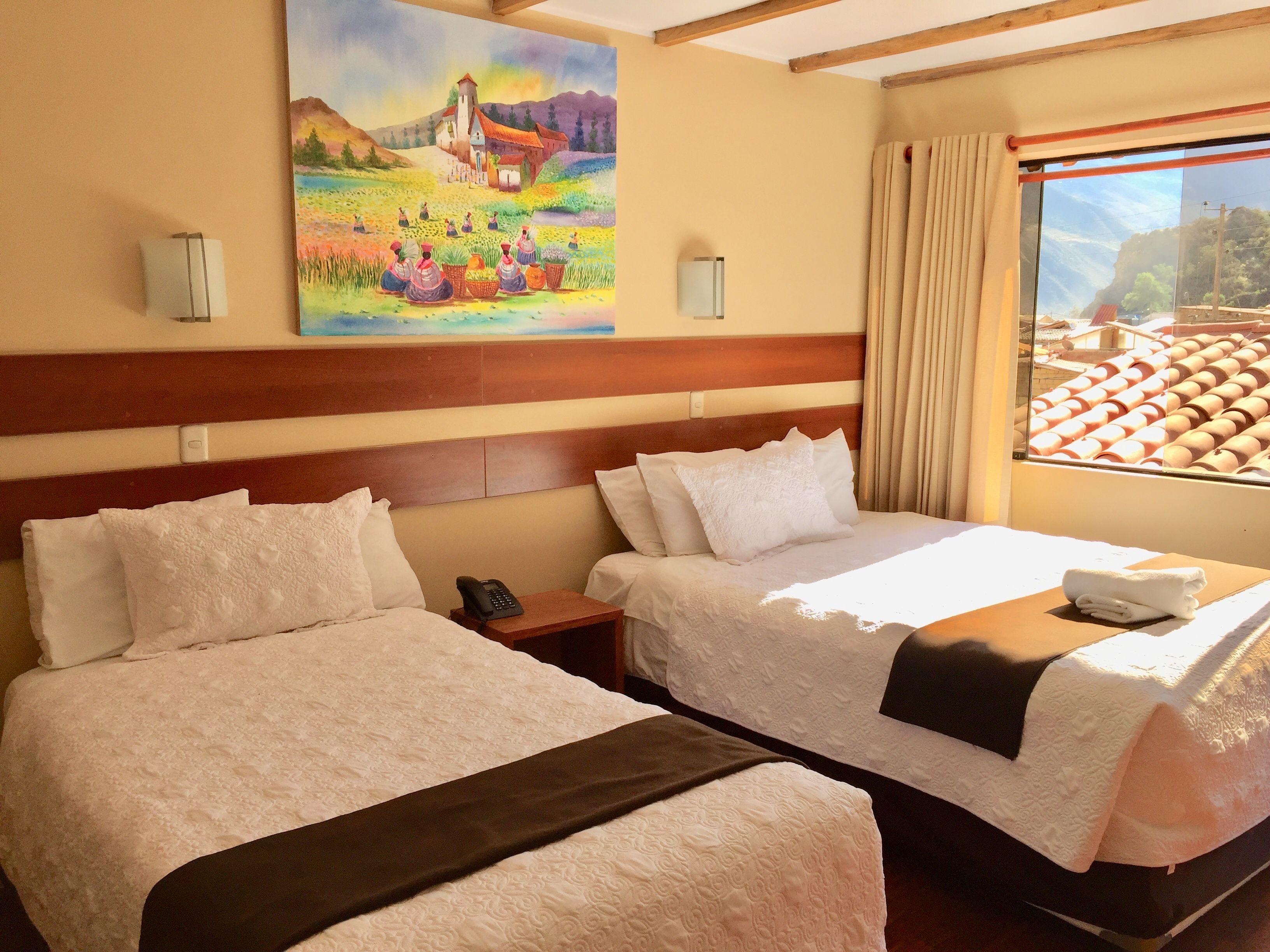 Habitación de hotel con dos camas, un cuadro en la pared, una ventana con vista a edificios y una mesita de noche con un teléfono.