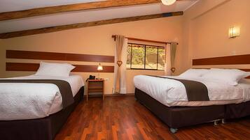 Una habitación con dos camas, suelo de madera, una mesita, una lámpara y una ventana con cortinas.
