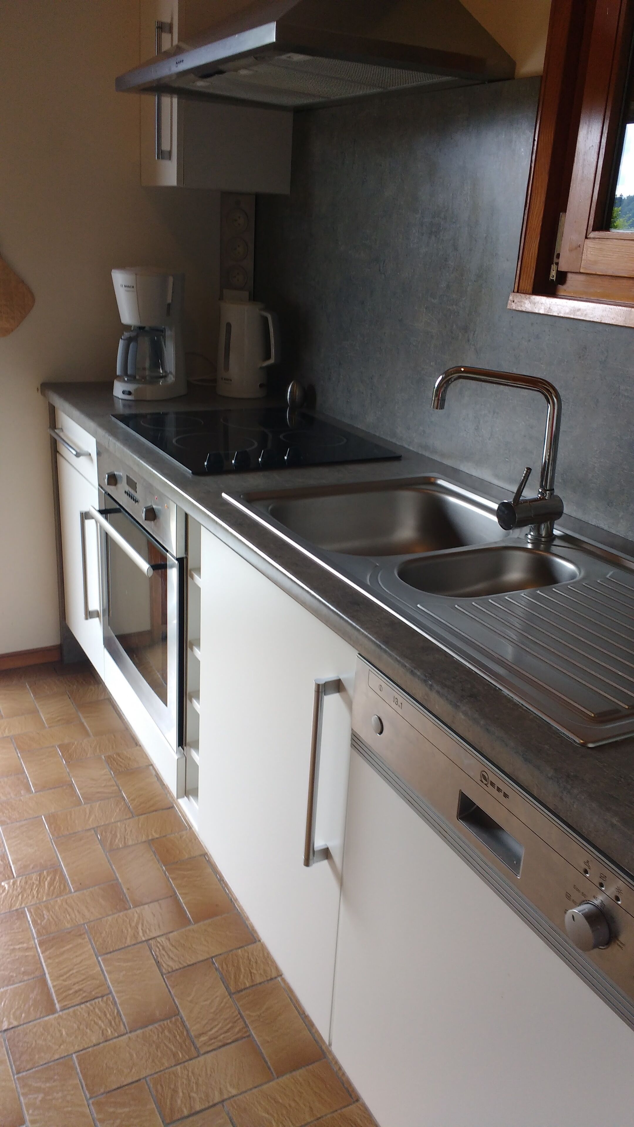 Una cocina moderna con un lavamanos de acero inoxidable, un horno empotrado y una cafetera.