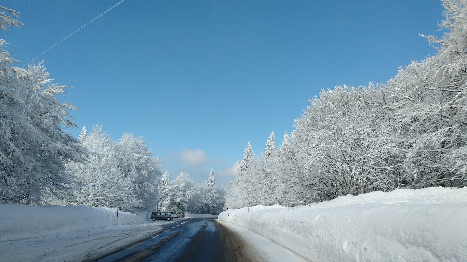 A snow-covered road flanked by trees under a clear blue sky.