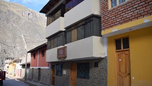 A street with buildings, including a two-story structure with a signboard, a yellow building with a wooden door, and a brick building with a window. - Ruinas View (Ollantaytambo)