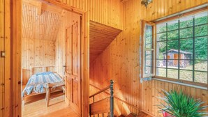 Un interior de madera con una cama, una silla, una escalera y una ventana con vistas al exterior.