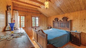 Un dormitorio de cabaña de madera con una cama, un aparador de madera, un escritorio con lámpara y una ventana.