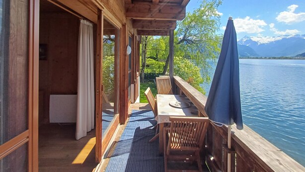 A wooden deck with a table and chairs, overlooking a lake with mountains in the background. - Waterfront Apartment 1 (Zell am See)