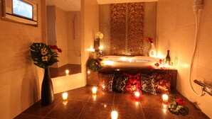 Un baño con bañera, ducha y tocador con espejo. Hay velas en el suelo y un jarrón con flores sobre el tocador.