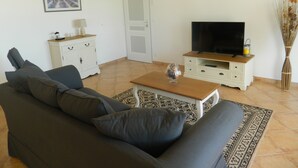 A living room with a sofa, a television on a wooden stand, a white cabinet, and a patterned rug. - Maison Grenat.  Vacation home with private pool, (Orgnac-l'Aven)