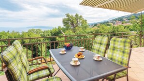 Eine Terrasse mit Tisch für zwei Personen, umgeben von karierten Stühlen, mit Blick auf eine malerische Landschaft mit Hügeln und einem Gewässer.