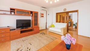 Ein modernes Wohnzimmer mit Flachbildfernseher, einer Holz-Unterhaltungseinheit, einem weißen Sofa und einer Blumenvase.