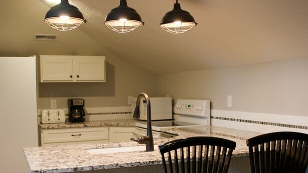 Una cocina con una isla central, dos sillas negras y una lámpara con tres luces.