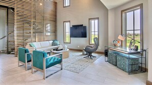 A spacious living room with a high ceiling, a modern sofa set, a glass coffee table, and a TV mounted on the wall. - The Luxe Lookout - Private Pool & Breathtaking Beach Views (Port Aransas)