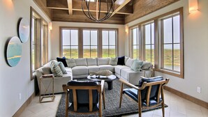 A spacious living room with a large sectional sofa, a coffee table, and two chairs. There are large windows providing a view of the outdoors. - The Luxe Lookout - Private Pool & Breathtaking Beach Views (Port Aransas)