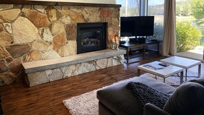A living room with a stone fireplace, a television, and a view of a lake. - 2025 Updates - Modern Townhome In Deer Valley With Shuttle Service (Park City)