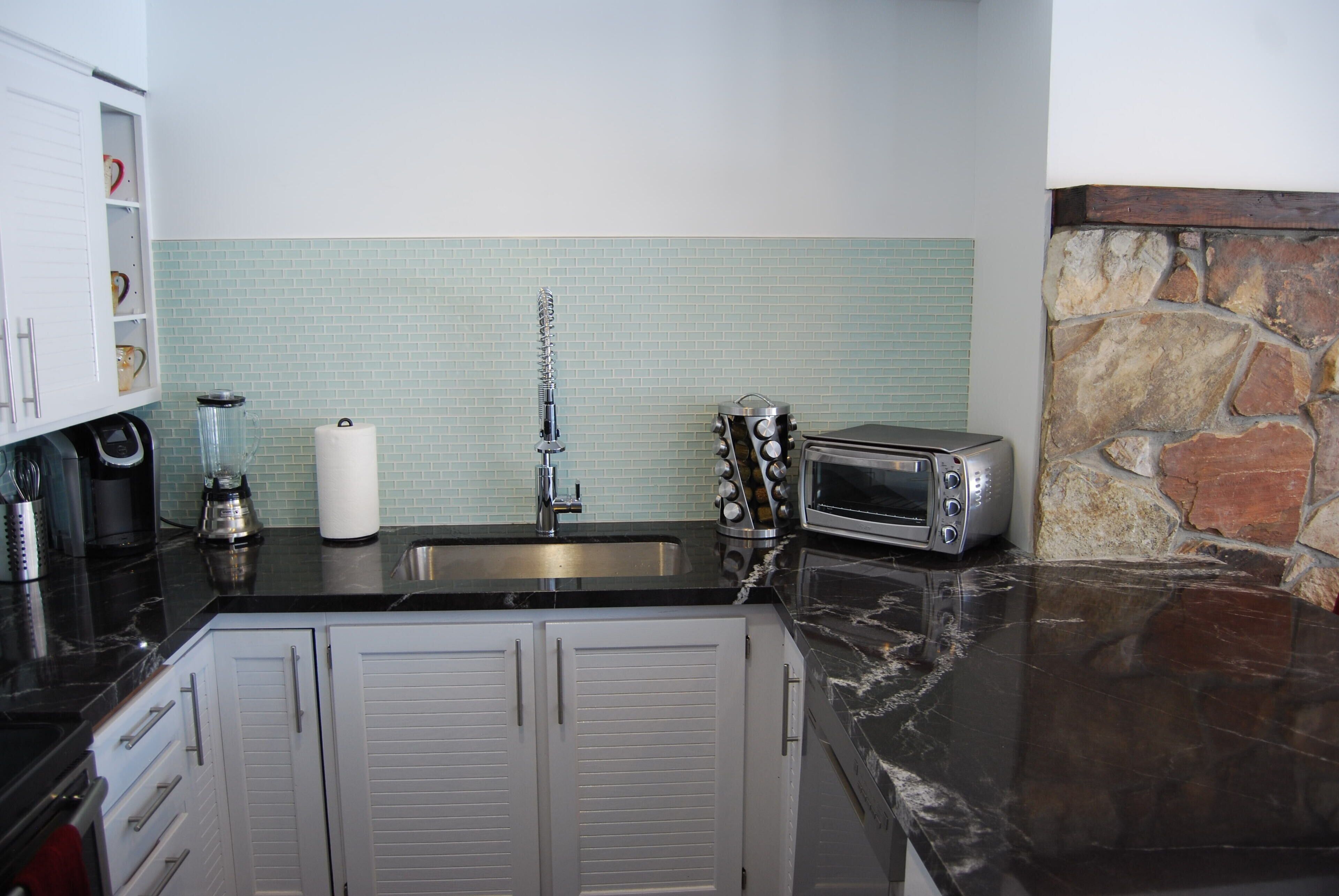 A kitchen with a black countertop, white cabinets, a stone backsplash, and a built-in oven.