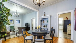 A dining area with a round table, four chairs, and a chandelier. There is a bookshelf with decorative items and a television in the background. - Downtown Historic Charm with Modern Comfort (Prescott)