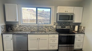A modern kitchen with white cabinets, a stainless steel dishwasher, a microwave, and an oven. - Downtown Historic Charm with Modern Comfort (Prescott)