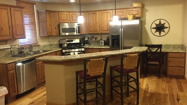 Una cocina con armarios de madera, electrodomésticos de acero inoxidable, una isla central con taburetes de bar y un adorno en forma de estrella en la pared.