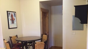Un comedor con una mesa y sillas de madera, un cuadro enmarcado en la pared y una puerta que da a otra habitación.